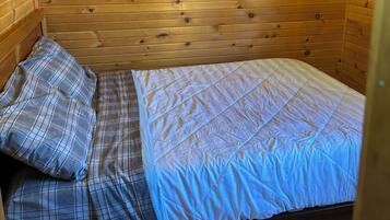 A wooden cabin room with a bed, wooden walls, and a ceiling with exposed beams.