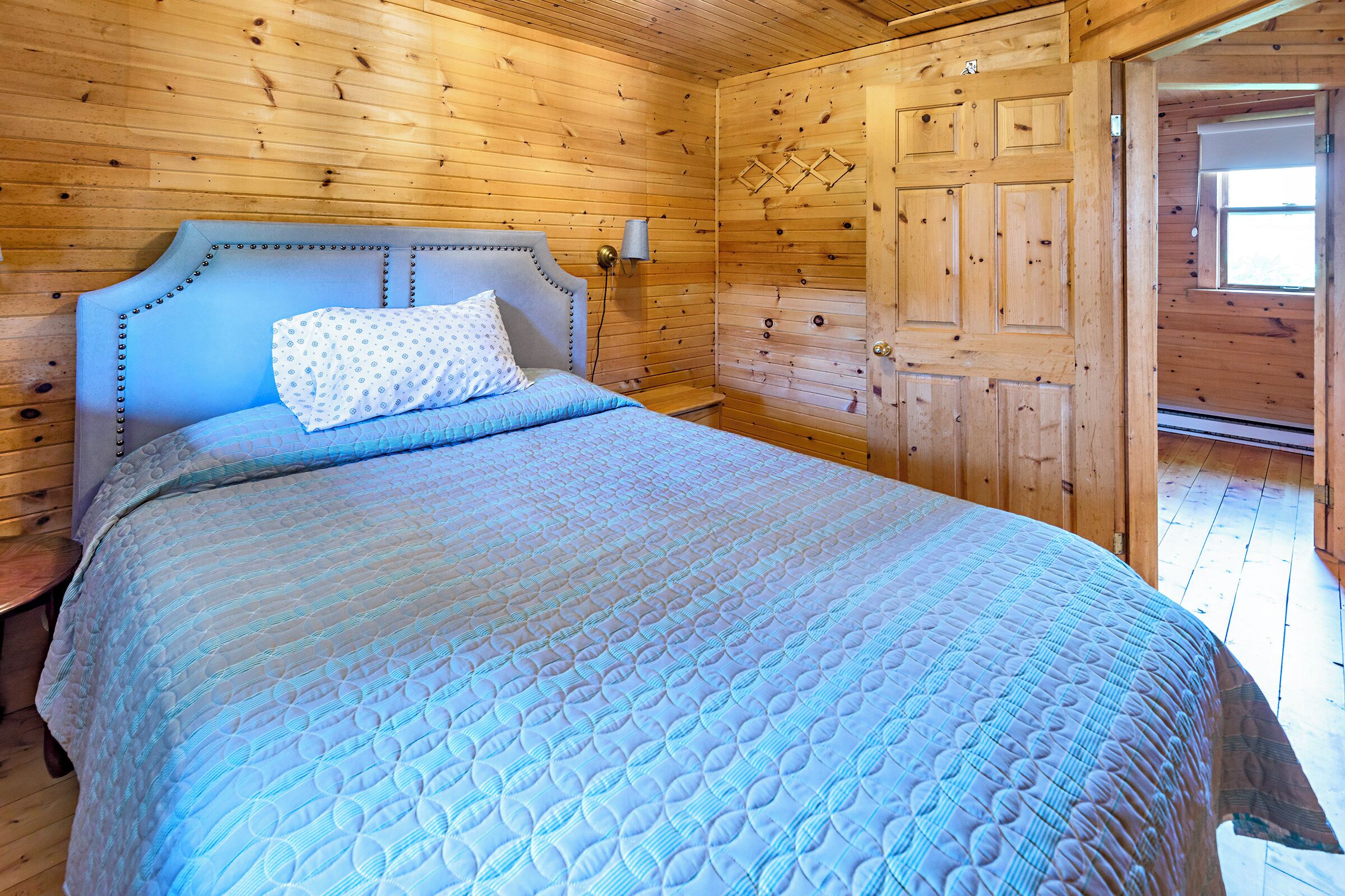 A wooden cabin room with a bed, a nightstand, and a wooden door.