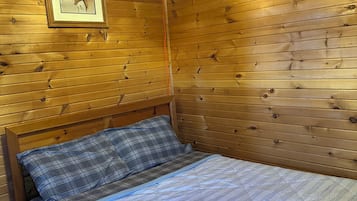 A wooden cabin room with a bed, a headboard, a framed picture on the wall, and wooden paneling.