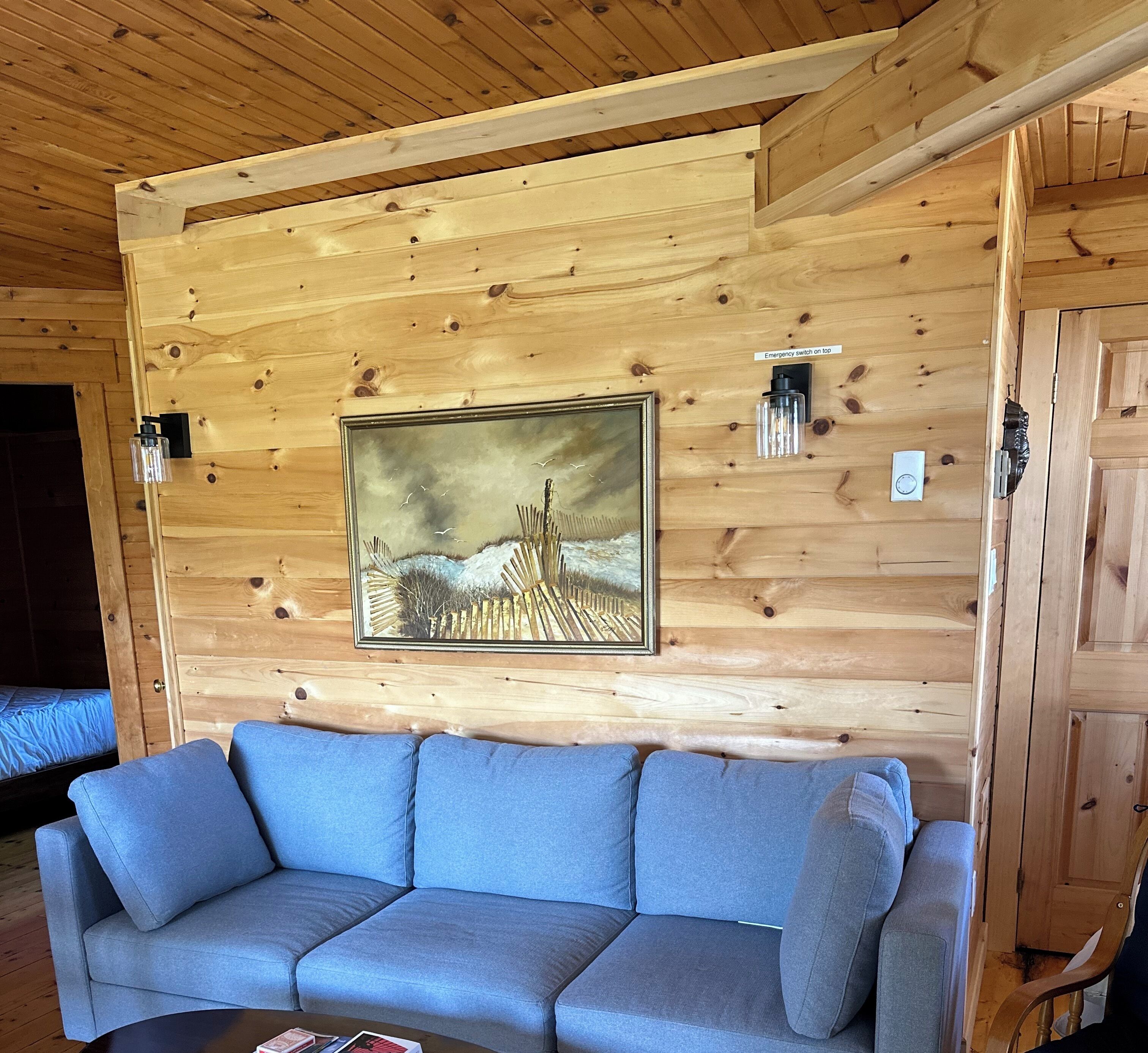 Een houten interieur met een blauwe bank, een lijst met een schilderij en een noodknop op de muur.