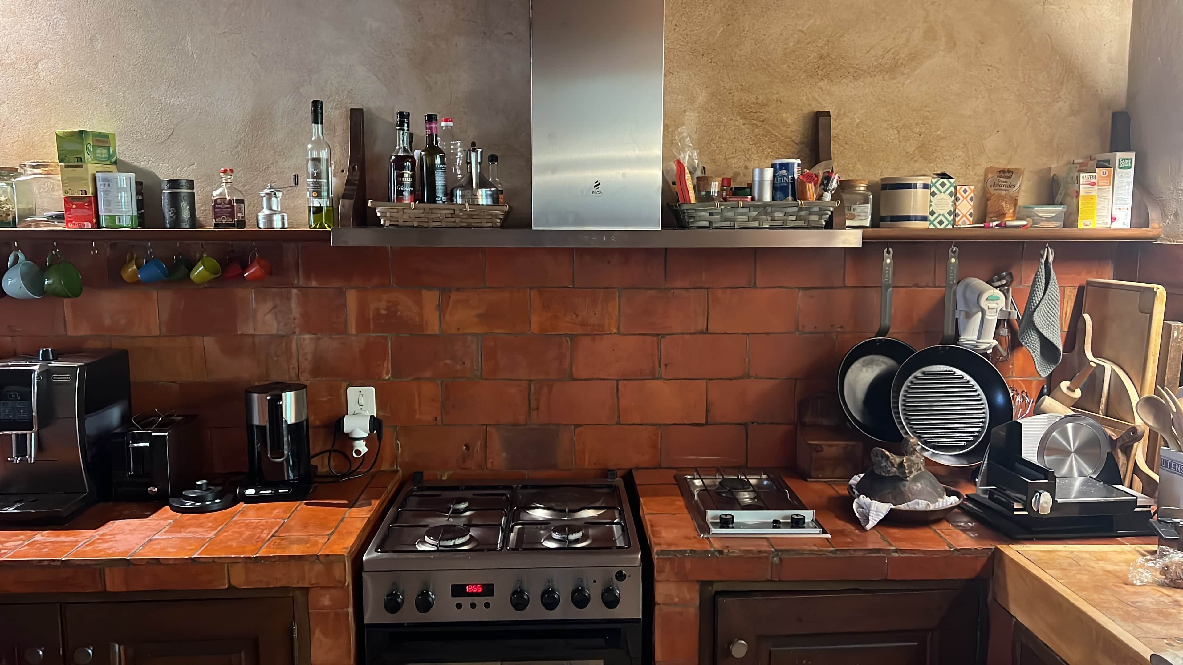 Una cocina con protector contra salpicaduras de ladrillo, una estufa a gas, una cafetera y diversos utensilios de cocina.