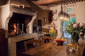 A rustic kitchen with a stone fireplace, wooden furniture, and a view of greenery outside. - The House in Provence (BONNIEUX)