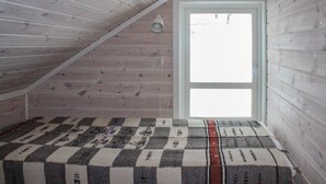 Ein kleiner Raum mit geneigtem Dach, Holzwänden und einer karierten Decke auf dem Boden.