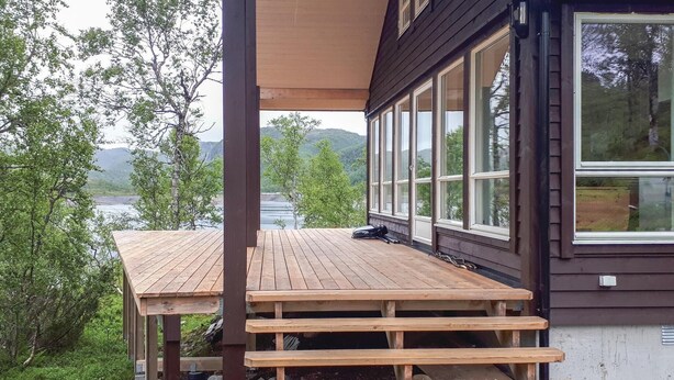 Eine Holzterrasse mit Tisch und Bänken, mit Blick auf einen See, Bäume und Hügel im Hintergrund.