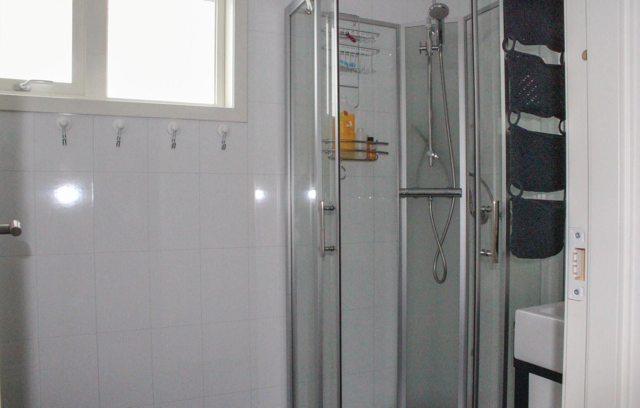 A glass-enclosed shower with a handheld showerhead and a wall-mounted faucet.