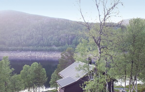 A cabin with a sloped roof, surrounded by trees and a lake. - Awesome home in Matre with kitchen (Matre)