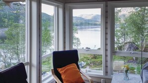 Ein Zimmer mit Seeblick und Bergblick, ein Sessel mit Kissen sowie ein kleiner Tisch mit Blumen in einer Vase.