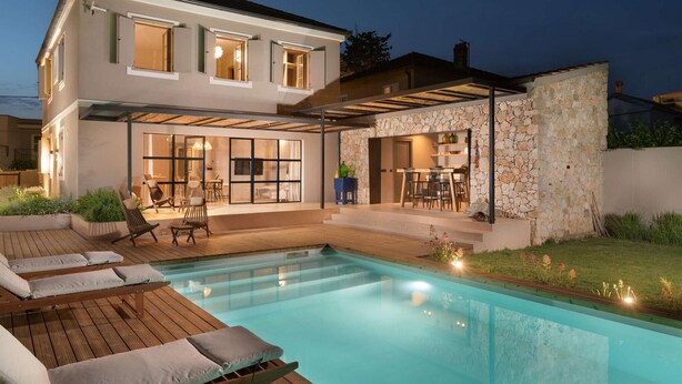 Una casa moderna con piscina, mobiliario exterior y una pared de piedra.