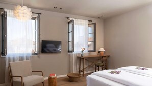 Un dormitorio con cama, una silla, un escritorio, un televisor y una ventana con cortinas.