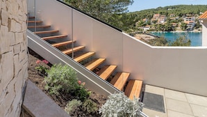 Eine moderne Treppe mit Holzboden, die zu einem Balkon mit Blick auf eine Küstenstadt und ein Gewässer führt.