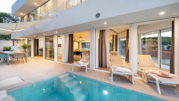 Ein modernes Haus mit Swimmingpool, Sitzgelegenheit im Freien und großen Fenstern.