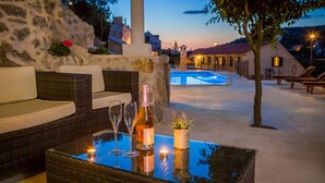 A cozy outdoor seating area with a glass table, two wine glasses, a bottle, and a candle. A pool is visible in the background. - Amazing home in Lozisca with WiFi (Lozisca)