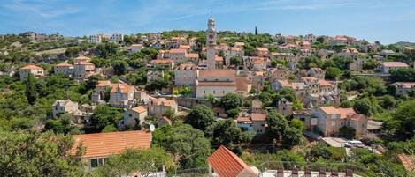 A hillside village with stone buildings, a prominent church, and a swimming pool area.