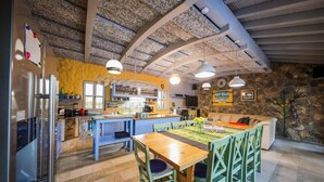 A modern kitchen with a dining area, stone walls, and a high ceiling with exposed beams.