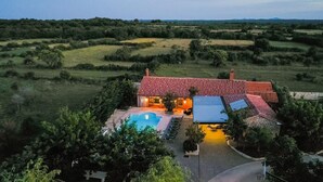 A house with a swimming pool, surrounded by greenery and hills.
