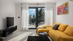 A modern living room with a sofa, a TV, and a balcony with outdoor furniture.