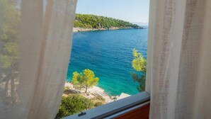Vista de una zona costera con mar azul cristalino, costa rocosa y una colina bordeada de árboles.