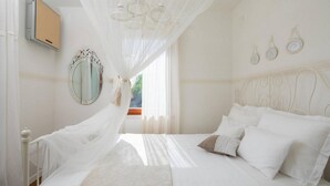 Un dormitorio con cama, mesita de noche, espejo y ventana con cortinas.