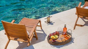 Escena junto a la piscina con sillas de madera y una bandeja con frutas y bebidas.