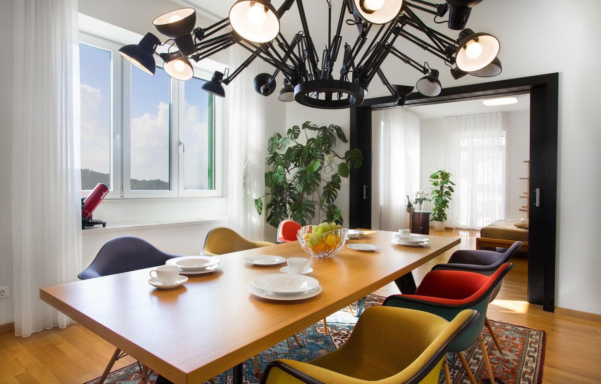 Un espace repas moderne avec une table en bois, des chaises colorées et un luminaire suspendu au plafond.