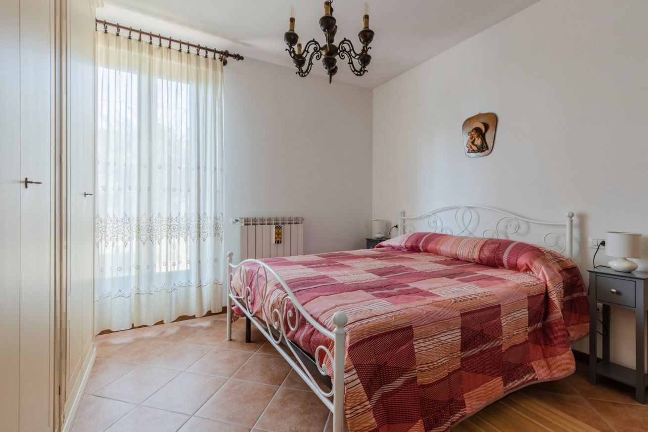Quarto com cama, mesa de cabeceira, candelabro, radiador e janela com cortinas.