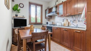 A kitchen with wooden cabinets, a dining table, chairs, a TV, a window, and a potted plant.