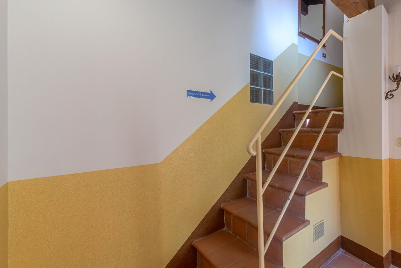 Una escalera con un letrero azul que indica dirección, una barandilla y una pared con una rejilla de ventilación.