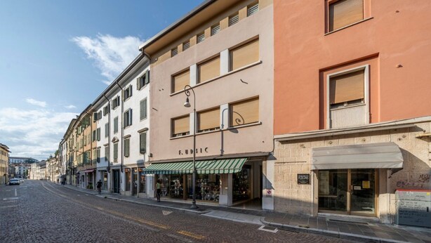 Une rue pavée bordée d’immeubles à plusieurs étages, dont l’un arbore une devanture portant l’inscription « FURRIC ».