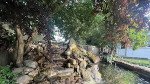 Un estanque con cascada de piedra y vegetación circundante.