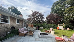 Un patio con mobiliario exterior, una fogata y luces colgantes.
