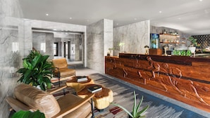 A lobby with marble walls, leather seating, a reception desk with a wooden sculpture, and a bar area with shelves of bottles and plants. - Wolfe's Hotel Moab (Moab)