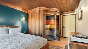 A bedroom with a bed, a wooden wardrobe, a bathroom with a mirror, and a small desk with a turntable. - Wolfe's Hotel Moab (Moab)