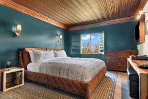 Un dormitorio con una cama grande, un cabecero de madera, una mesita de noche, un aparador y una ventana con persianas.