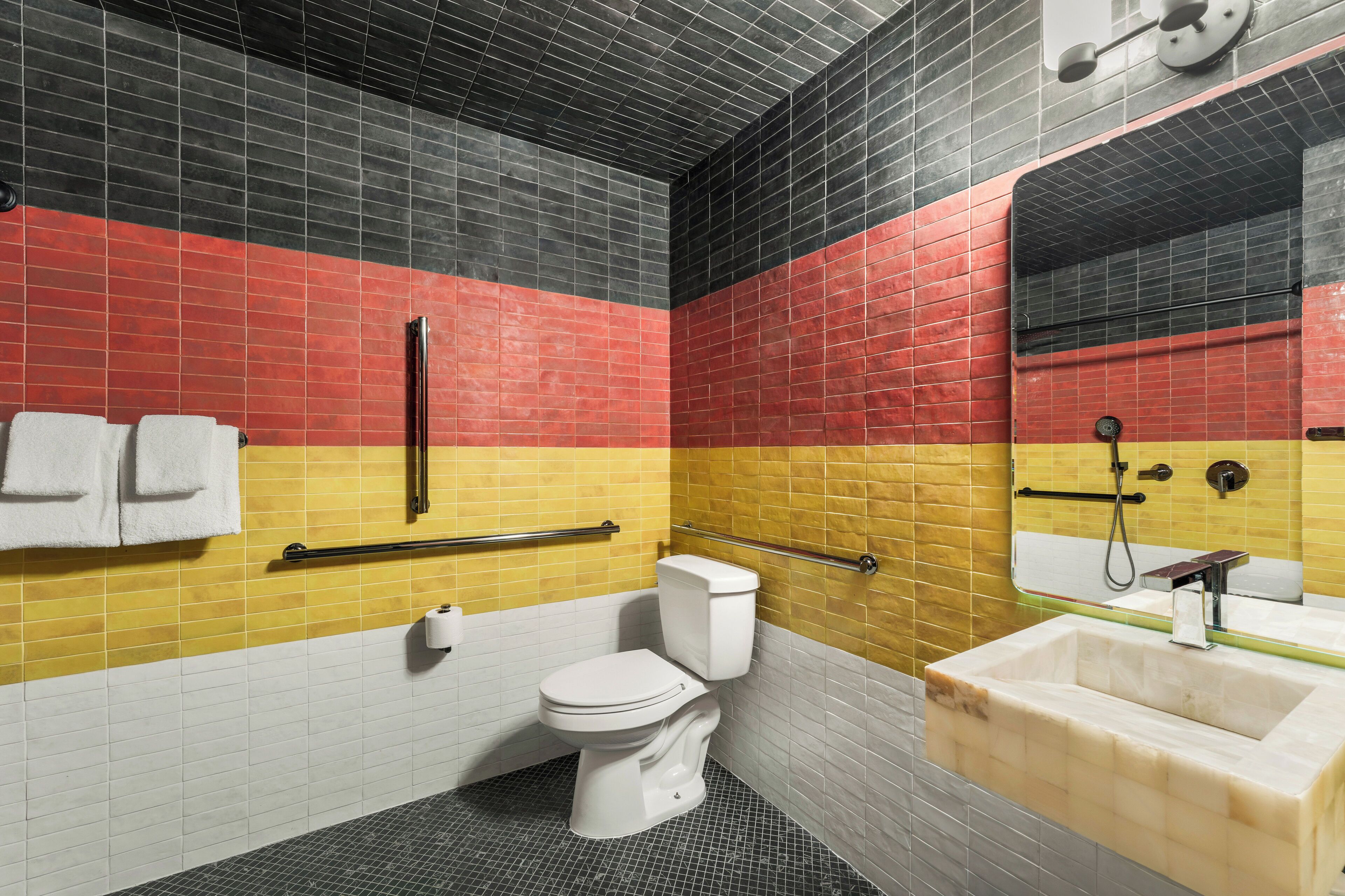 Een badkamer met een wit toilet, een wastafel en een spiegel. Er is een handgreep en een handdoekhouder.
