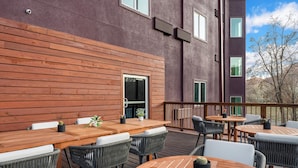 An outdoor patio with wooden tables and chairs, a view of a building with large windows, and a clear sky. - Wolfe's Hotel Moab (Moab)