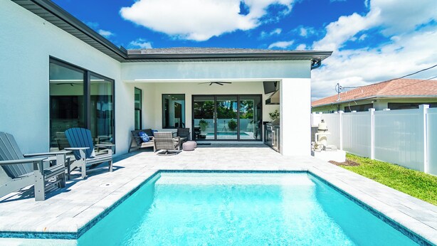 A modern house with a swimming pool, large windows, and a patio area with outdoor furniture.