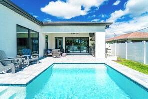 Una casa moderna con piscina, ventanas amplias y un patio con mobiliario exterior.