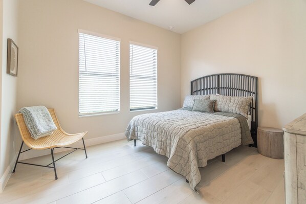 Un dormitorio con cama, una silla y dos ventanas.