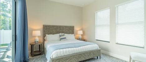 A bedroom with a bed, two bedside lamps, a ceiling fan, and a view of the outdoors.