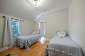 Een slaapkamer met twee enkele bedden, een raam met gordijnen en een plafondlamp.