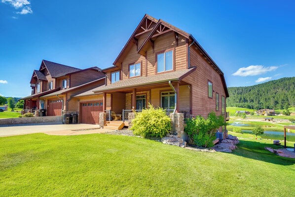 A two-story house with a large porch, a stone foundation, and a well-maintained lawn. - Hot Tub + Golf Course Views: Luxe Sturgis Home! (Sturgis)