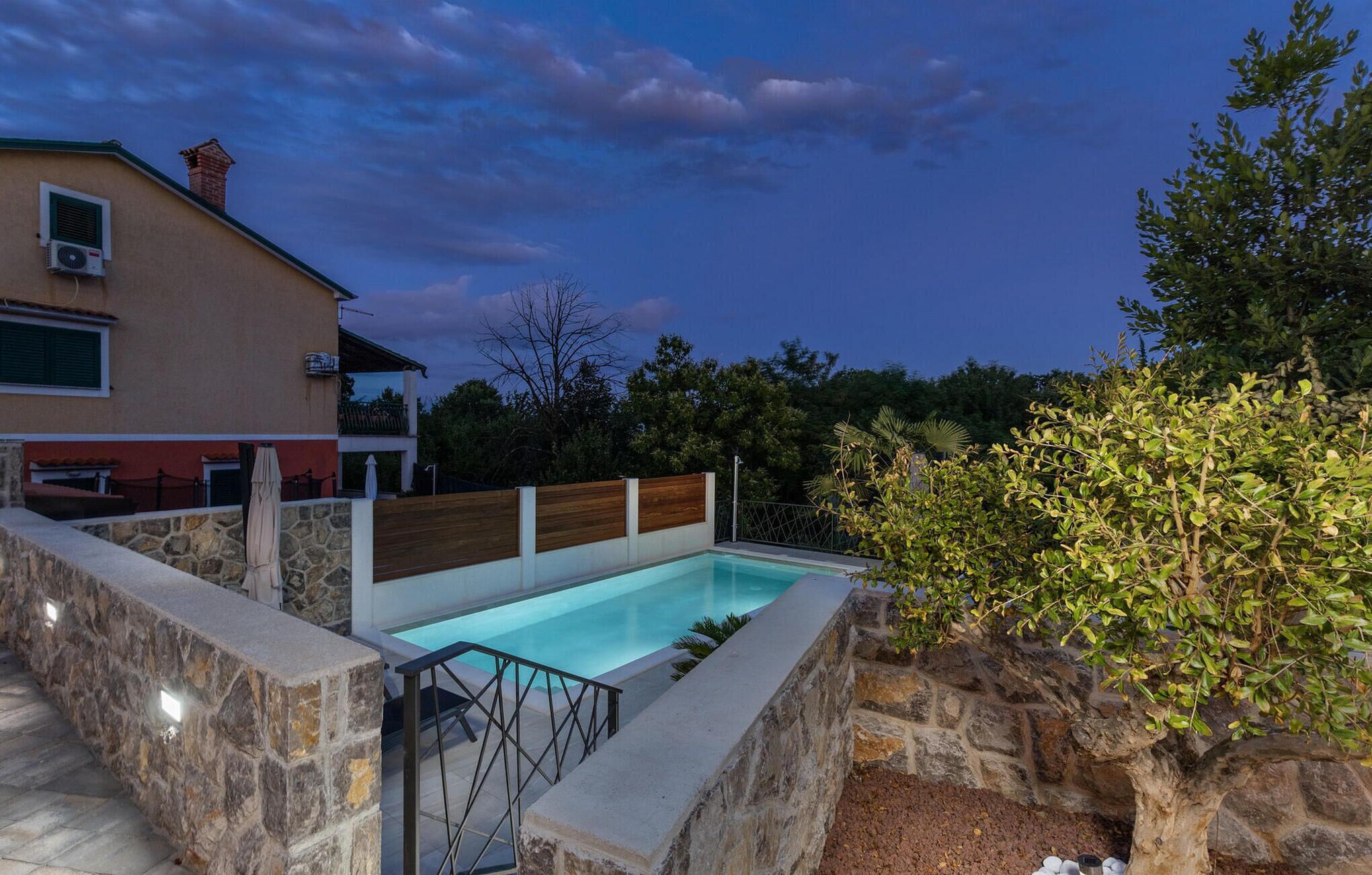 Una piscina con muros de piedra, una terraza de madera y una escalera de piedra que lleva a una zona cubierta.