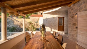 A wooden table with chairs and a vase of dried plants in a covered outdoor area with stone walls and a wooden door. - Villa Bea (Dvor Pitve Villa B) (Jelsa)