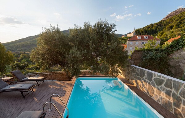 A swimming pool with a wooden deck, lounge chairs, and a stone wall. - Villa Bea (Dvor Pitve Villa B) (Jelsa)