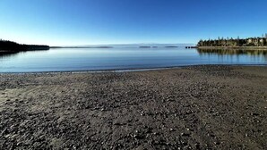 Un lac paisible, avec une rive de galets et une île boisée qui se profile à l’horizon.