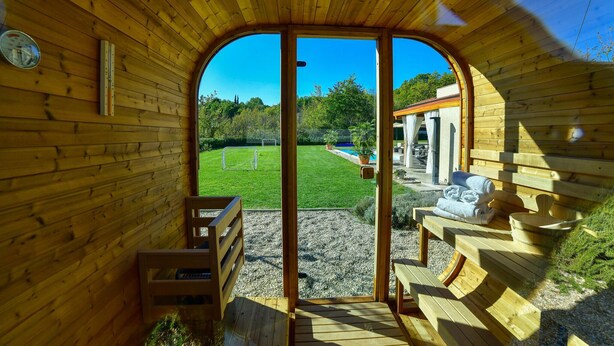 A wooden structure with a large arched doorway leading to an outdoor area with a pool, seating, and a garden.