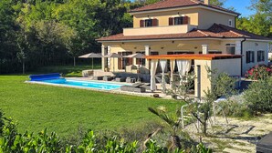 A two-story house with a swimming pool, outdoor furniture, and a garden.