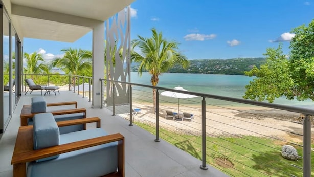 Uma varanda com assentos, vista para a praia e palmeiras.