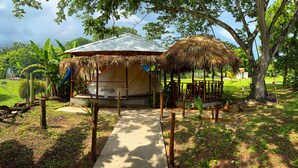 A thatched-roof structure with a metal roof, surrounded by a fenced garden area with a concrete pathway leading to it.