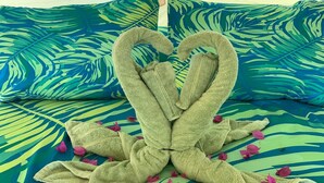 A bed with a tropical leaf-patterned bedspread and two towels arranged in a heart shape.